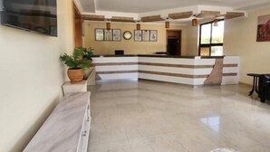 Un hall d’hôtel avec un comptoir d’accueil, un téléviseur à écran plat fixé au mur, une plante en pot et une table en marbre.