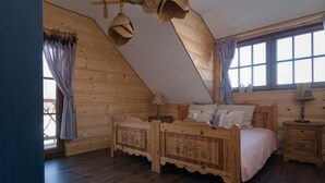 Un dormitorio de madera con techo inclinado, una cama con cabecera decorativa, una mesita de noche y una ventana con cortinas.