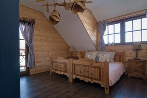 Ein Schlafzimmer aus Holz mit schrägem Dach, einem Bett mit dekorativem Kopfteil, einem Nachttisch und einem Fenster mit Vorhängen.
