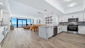 Eine moderne Küche mit weißen Schränken, ein Essbereich mit Holzmöbeln und Blick auf den Ozean.