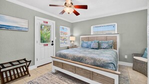 Ein Schlafzimmer mit Bett, Deckenventilator, Tür, Fenster, Nachttisch, Babybett und Korbstuhl.