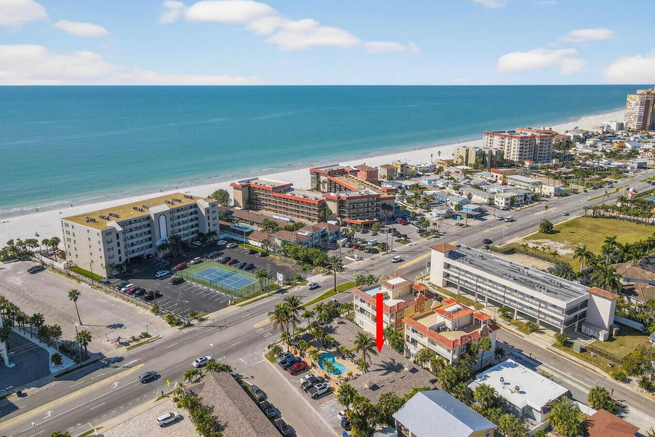 Vue aérienne d’un complexe hôtelier situé sur la côte, avec une plage, des parkings et une piscine.