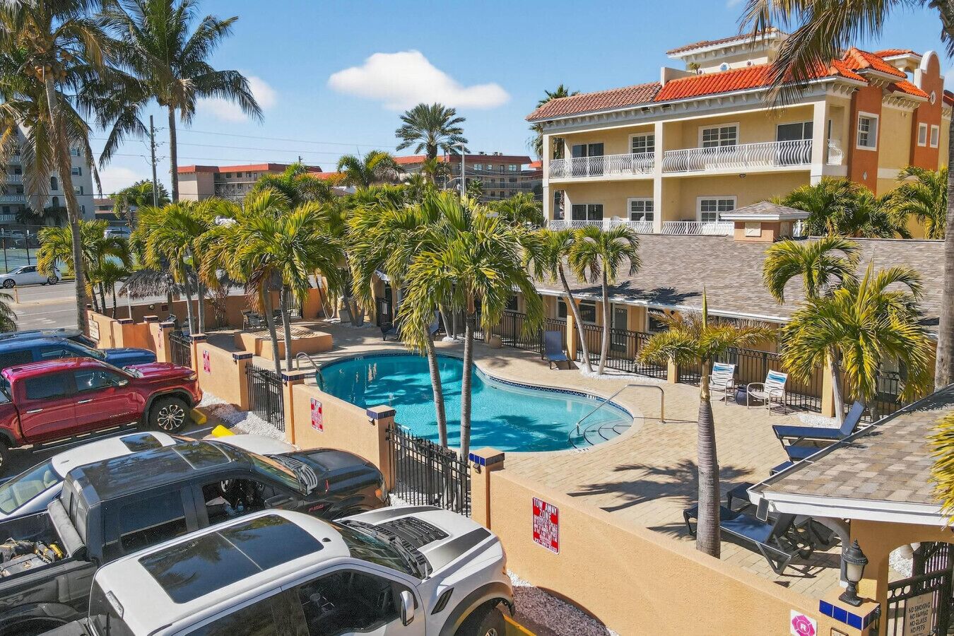 A hotel with a swimming pool, palm trees, and parked cars.