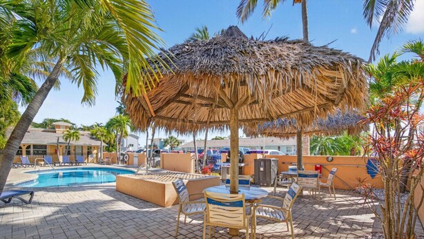 A pool area with lounge chairs, a thatched umbrella, and palm trees. - Coconut Villas Suite 5 (Redington Shores)