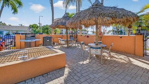 An outdoor patio with thatched umbrellas, seating, and a grill area. - Coconut Villas Suite 5 (Redington Shores)