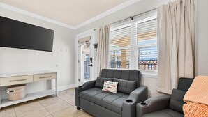 A modern living room with a sofa, a TV, a window with curtains, and a balcony view. - Coconut Villas Suite 5 (Redington Shores)