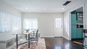 Un comedor con mesa, sillas y un banco. Se ve una cocina a través de una puerta abierta.