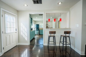 Un couloir avec une porte, un coin cuisine avec des meubles de couleur turquoise et deux tabourets.