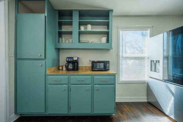 Une cuisine avec des meubles de couleur turquoise, un four à micro-ondes et une machine à café posés sur le plan de travail.