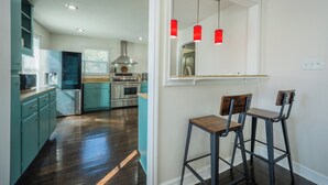 Una cocina con electrodomésticos de acero inoxidable, armarios color turquesa y un taburete de bar de madera.