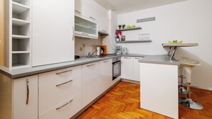 Een moderne keuken met witte kasten, een visgraatparketvloer, een ingebouwde magnetron en een klein eiland met een spoelbak en krukken.
