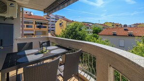 Een balkon met een tafel en stoelen, met uitzicht op een woongebied met gebouwen en bomen.