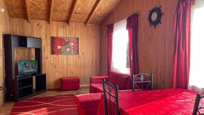 A wooden interior with a red sofa, a dining table, and a television on a wooden shelf.