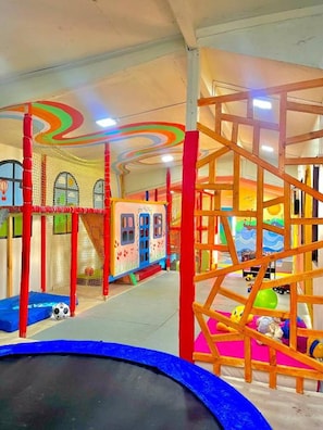 Een speelruimte met een trampoline, klimconstructies en een speelhuisje met net.