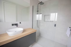 A modern bathroom with a large mirror, a white vessel sink, a shower with a handheld showerhead, and a towel rack. - The Modern on Longley - 4 Bedroom Townhouse (Alfredton)