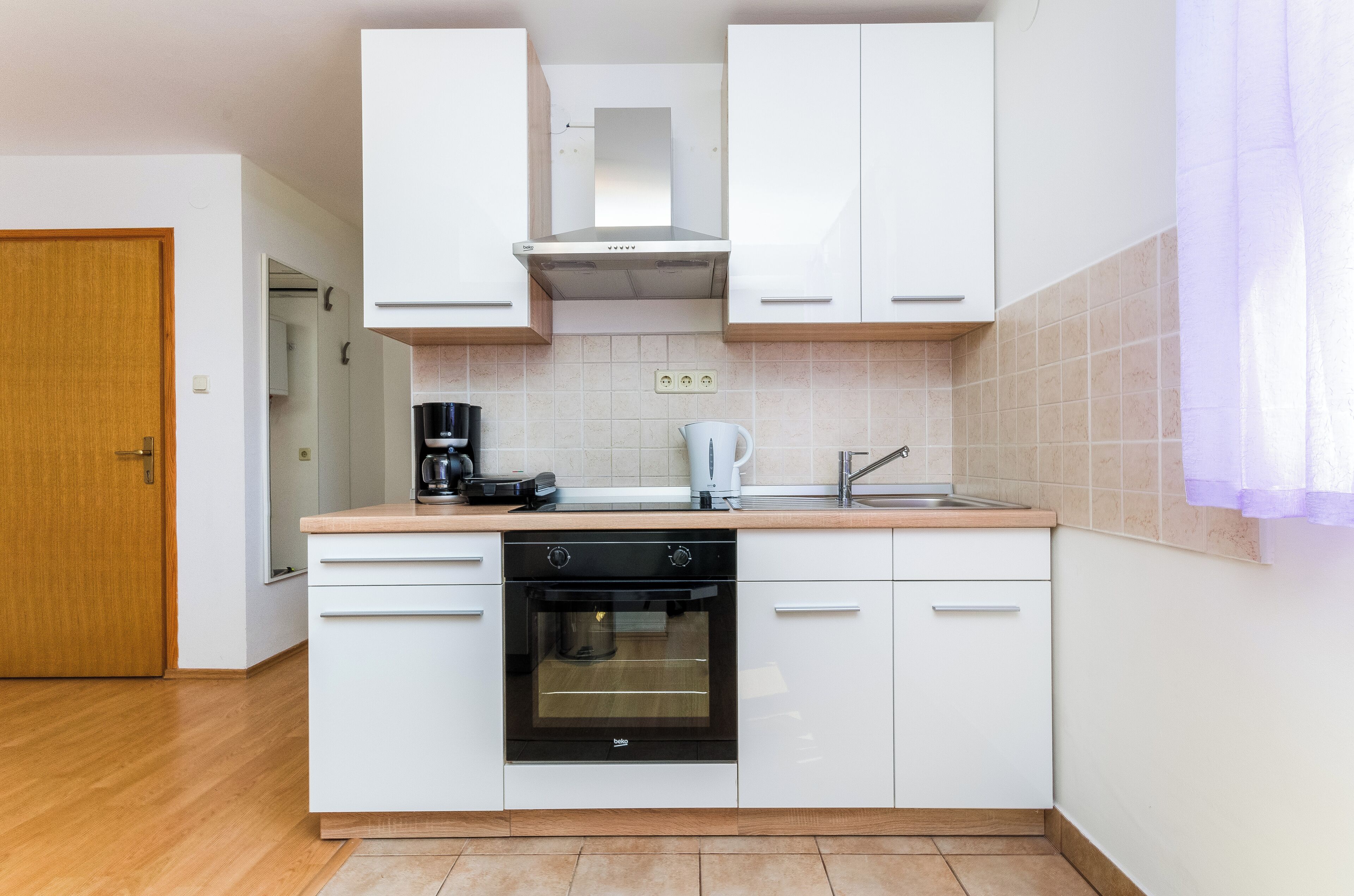 Eine moderne Küche mit weißen Schränken, einem Backofen, einer Kaffeemaschine und einem Wasserkocher.