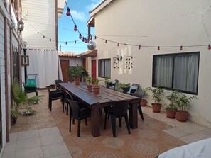 Un patio al aire libre con una mesa y sillas de madera, rodeado de plantas en macetas.