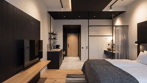 A modern hotel room with a wooden bench, a bed, a TV, a desk with a coffee machine, and a bathroom with a sink and mirror. - Santa's Hotel Noelle (Rovaniemi)