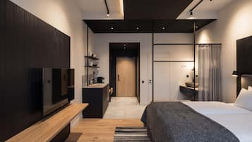 Quarto de hotel moderno com um banco de madeira, uma cama, uma TV, uma escrivaninha com máquina de café e um banheiro com pia e espelho.