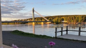 A river with a bridge, a wooden deck, and pink flowers in the foreground. - Santa's Hotel Noelle (Rovaniemi)