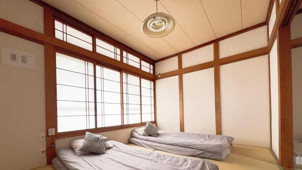 Ein traditioneller japanischer Raum mit Tatami-Boden, zwei niedrigen Betten mit Kissen, einem Shoji-Bildschirm und einer Deckenleuchte.