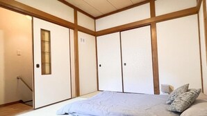 Ein traditioneller japanischer Raum mit Tatami-Bodenbelag, einem niedrigen Bett mit blauer Matratze und verschiebbaren Shoji-Schiebetüren.