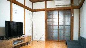 Ein Wohnzimmer mit Fernseher auf einem Holzständer, einer Schiebeglastür und einem grauen Sofa.