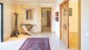 A hallway with a patterned rug, a mirror, a table with a lamp, and a door leading to another room. - VILLA IRLANDAIS (Alvor)