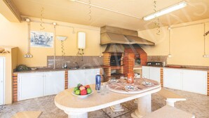 A kitchen with a brick oven, white cabinets, a table with a bowl of fruit, and a bench. - VILLA IRLANDAIS (Alvor)