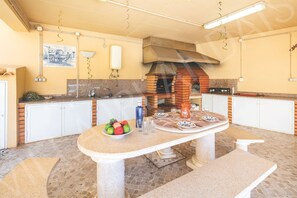 Eine Küche mit Backofen, weißen Schränken, einem Tisch mit Obstschale und einer Bank.