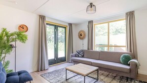 A modern living room with a sofa, a coffee table, a potted plant, and a large window with curtains. - Serene Ewijk Abode by the Lake (Ewijk)