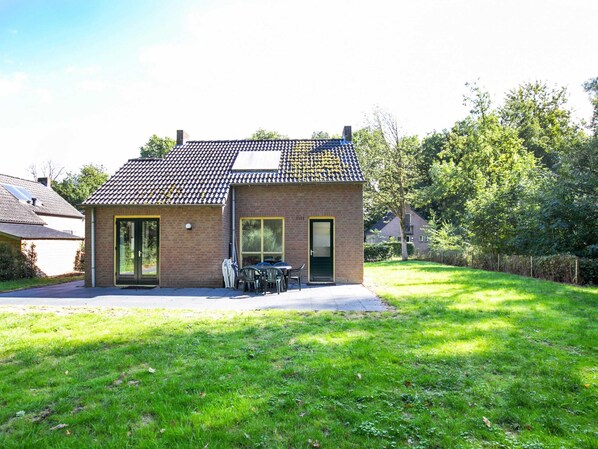 Une petite maison en briques avec un toit en tuiles, une porte d’entrée et une terrasse aménagée avec du mobilier d’extérieur.