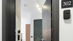 A modern hallway with a dark wooden door, a number sign '302', and a light-colored floor. - Tower 15 | Family Studio 302 (Thessaloniki)