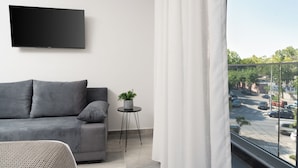 A modern living room with a grey sofa, a small side table with a plant, and a mounted TV. - Tower 15 | Family Studio 302 (Thessaloniki)