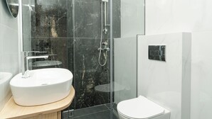 A modern bathroom with a white sink, a glass-enclosed shower, and a toilet. - Tower 15 | Family Studio 302 (Thessaloniki)