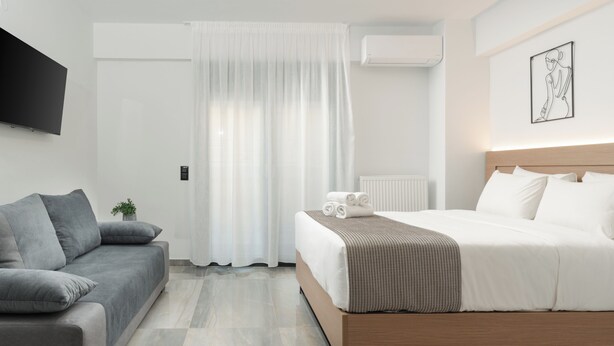 A modern hotel room with a bed, a sofa, a flat-screen TV, and a window with sheer curtains. - Tower 15 | Family Studio 302 (Thessaloniki)