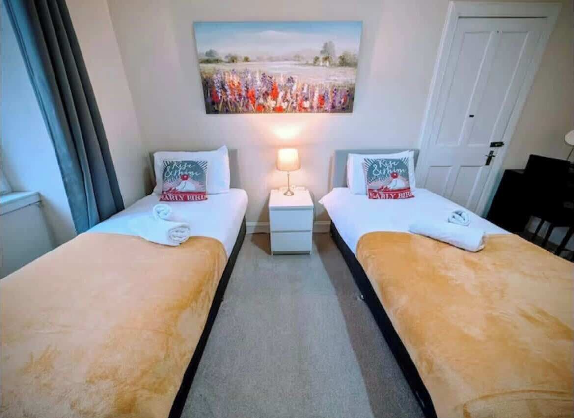 A hotel room with two beds, a nightstand, a lamp, and a painting on the wall.