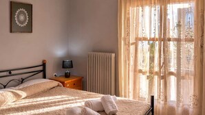A bedroom with a bed, a nightstand, a lamp, a radiator, and a window with curtains. - Matroni s House - Seafront Getaway in Monemvasia (Monemvasia)