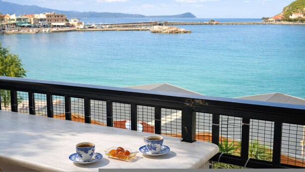A balcony with a table set for two, overlooking a calm sea and distant buildings. - Matroni s House - Seafront Getaway in Monemvasia (Monemvasia)