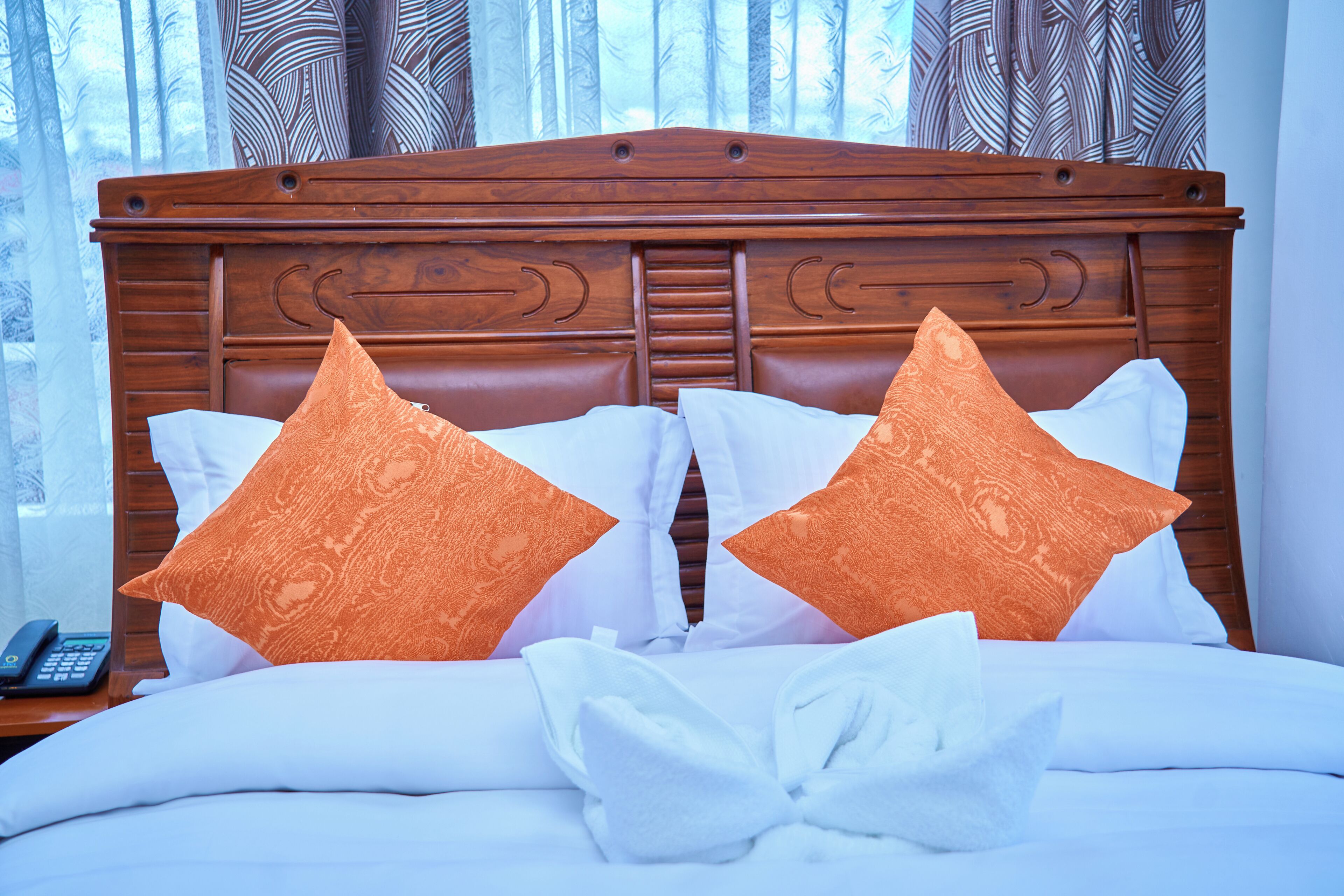 A neatly made bed with a wooden headboard, white bedding, and two orange pillows.