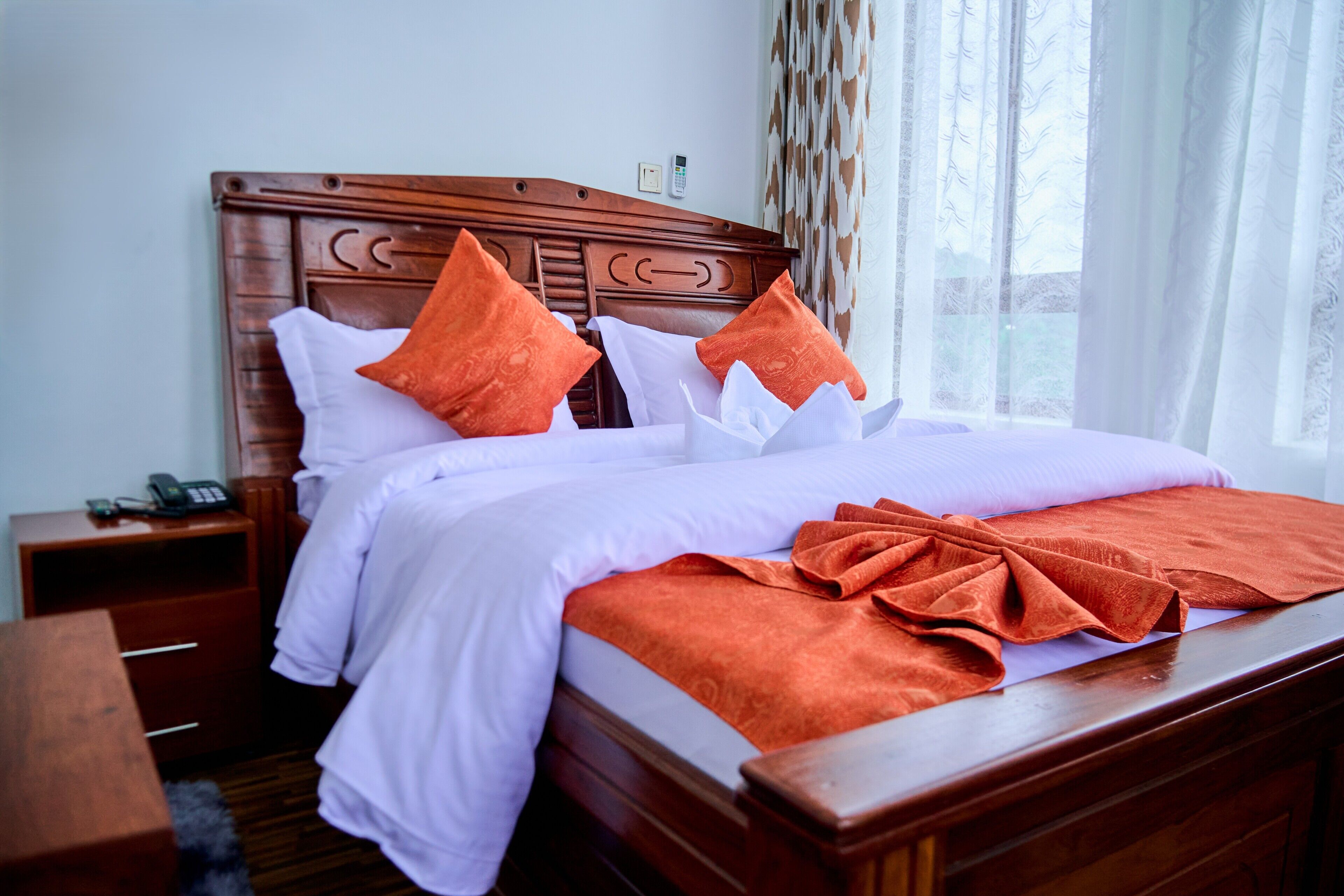 A hotel room with a wooden headboard, a bedside table with a phone, and a window with curtains.