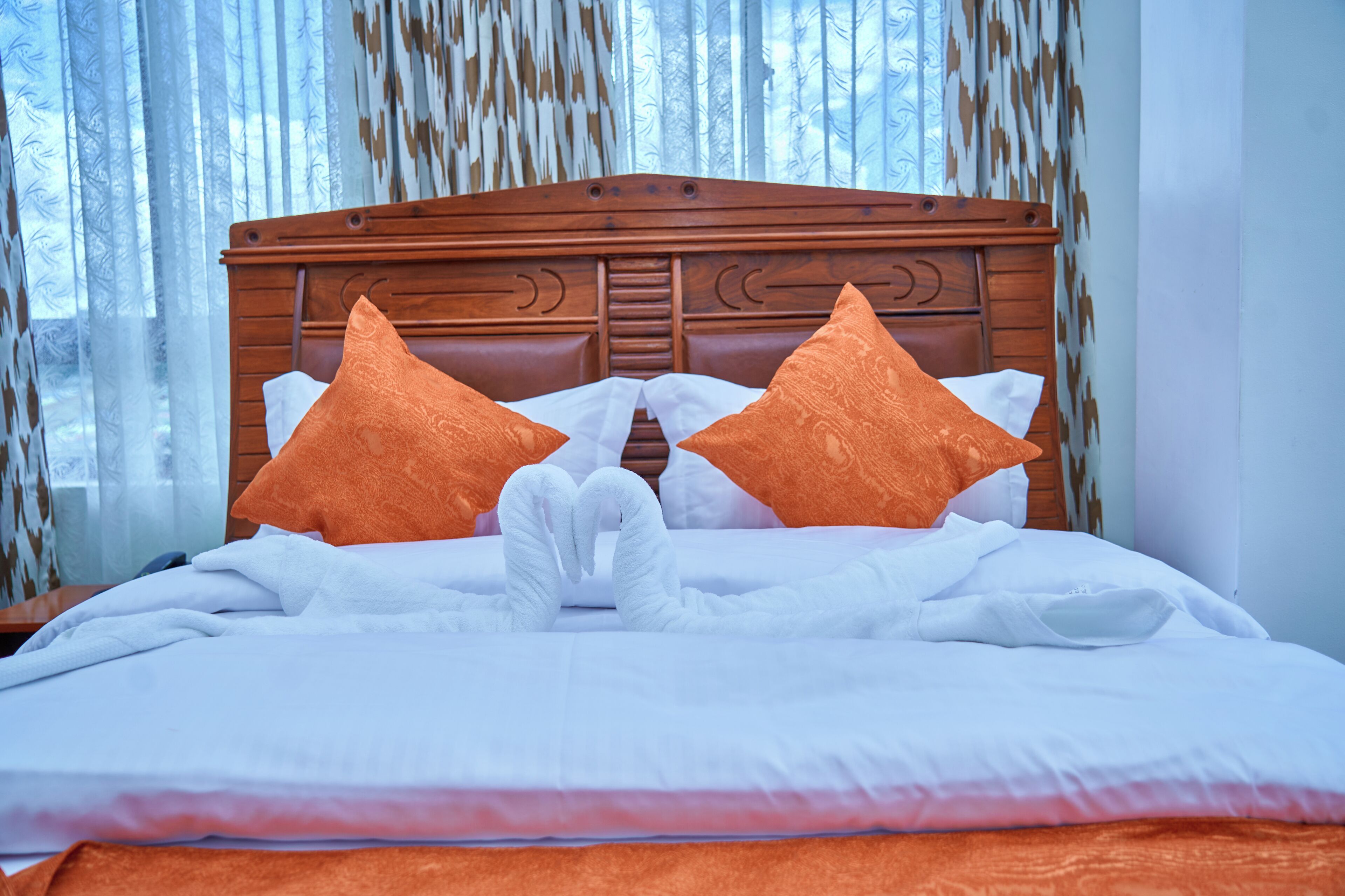 A neatly made bed with two pillows, a wooden headboard, and a window with curtains.