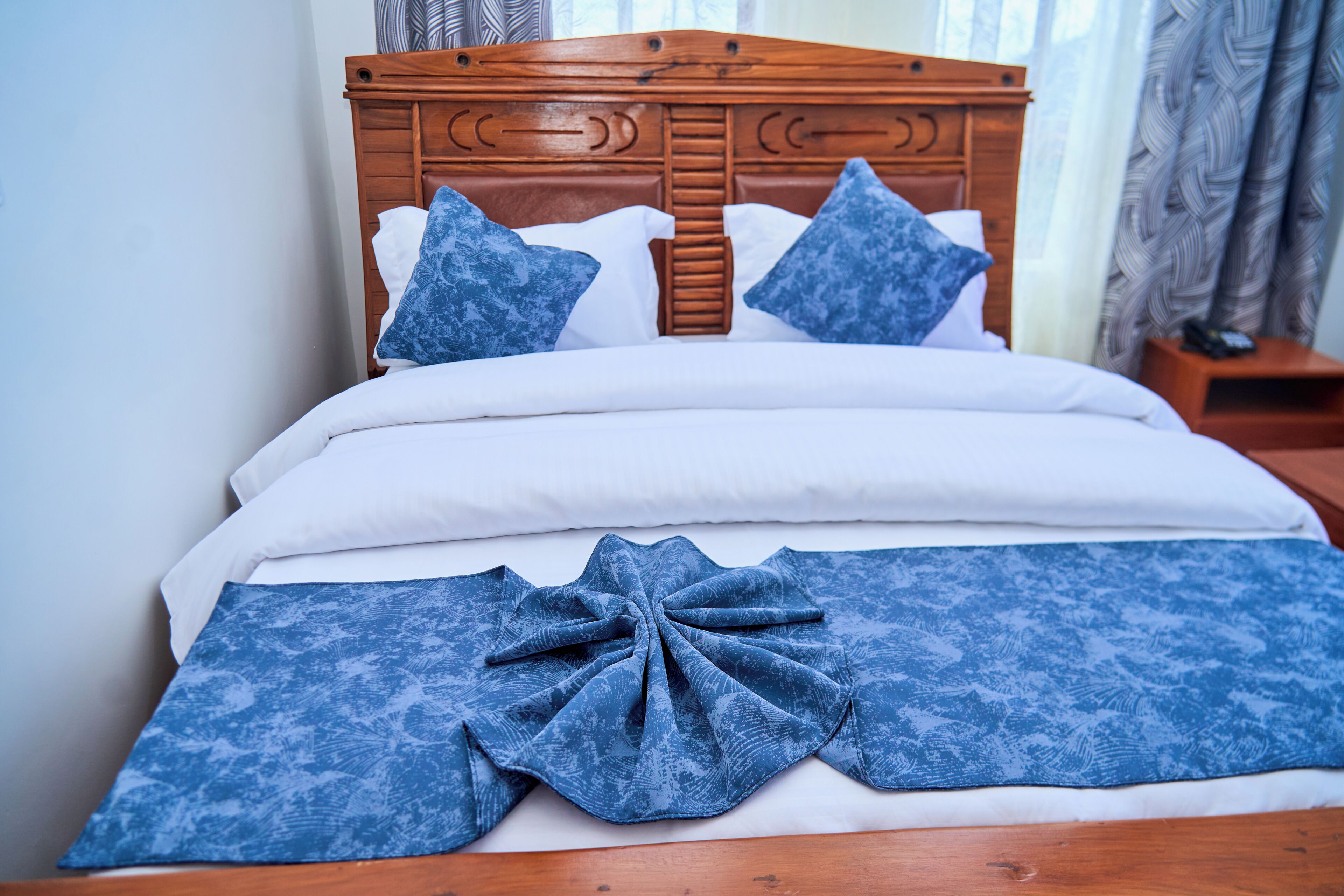 A neatly made bed with a wooden headboard, white bedding, and blue patterned pillows.
