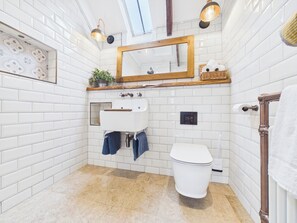 A bathroom with white subway tiles, a white toilet, a sink with a wooden countertop, a mirror, and two wall-mounted lights. - Tor Farm (Camelford)