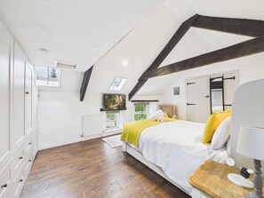 A bedroom with a sloped ceiling, a bed with a yellow blanket, a wooden floor, a window with a view, and a radiator. - Tor Farm (Camelford)
