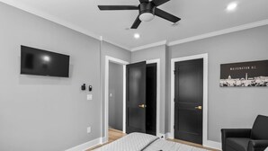 Ein Schlafzimmer mit einem Bett, einem Deckenventilator, einem Fernseher und einer Tür zu einem anderen Raum.