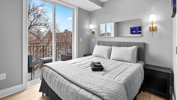 Ein modernes Schlafzimmer mit einem großen Bett, einem Balkon mit Aussicht und einem Nachttisch mit Lampe.