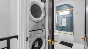 Une buanderie équipée de deux lave-linge Whirlpool, d’une cabine de douche carrelée et de toilettes blanches.