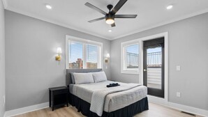 Une chambre à coucher comprenant un lit, des tables de chevet, un ventilateur de plafond et deux fenêtres équipées de stores.