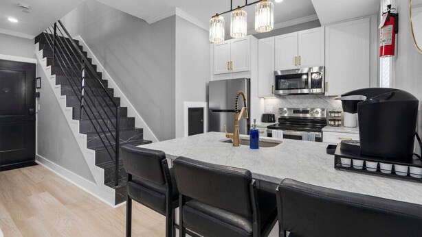 Une cuisine moderne avec un plan de travail en marbre, des chaises noires, des appareils électroménagers en acier inoxydable et un escalier noir.